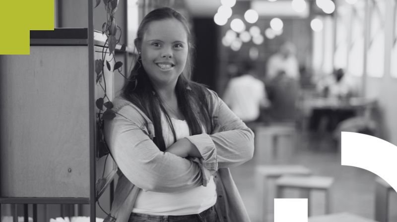 Foto de una mujer joven con sndrome de down, sonriente y en actitud empoderada con los brazos cruzados sobre el pecho